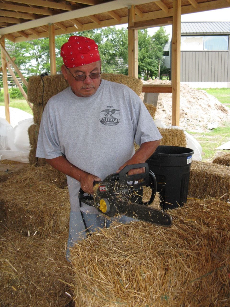 Leonard (Lenny) Lone Hill is shown carving a notch for a post with a chainsaw. He is a building trades instructor at Oglala Lakota College at the Pine Ridge Reservation and is one of the participants completing the 12 credit certificate in straw bale building taught by Laura Bartels.